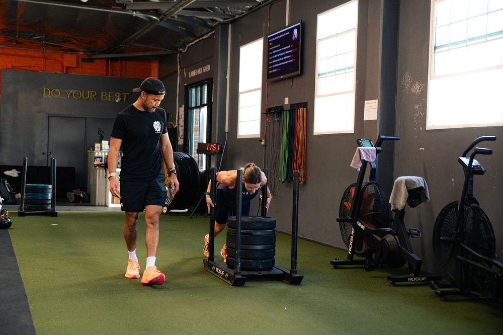 A Ganbatte coach walking the turf while an athlete pushes a sled